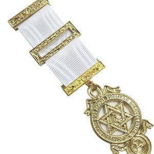 Puede incluir: Pendiente masónico de oro con una cinta blanca y una estrella de seis puntas con el texto "Deo Regni Fidelitas Honoribus Benevolentia" alrededor de la estrella.