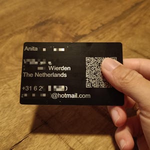 Op de afbeelding: Zwarte visitekaart met witte tekst. De tekst luidt "Anita", een telefoonnummer, een e-mailadres en "Wierden, Nederland". Een QR-code bevindt zich in de rechterbovenhoek.