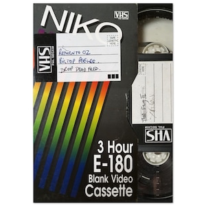 Könnte beinhalten: Ein schwarzes VHS-Band mit einem regenbogenfarbenen Streifenmuster. Das Band ist mit "3 Hour E-180 Blank Video Cassette" beschriftet. Das Etikett enthält auch den Text "VHS PAL SECAM".