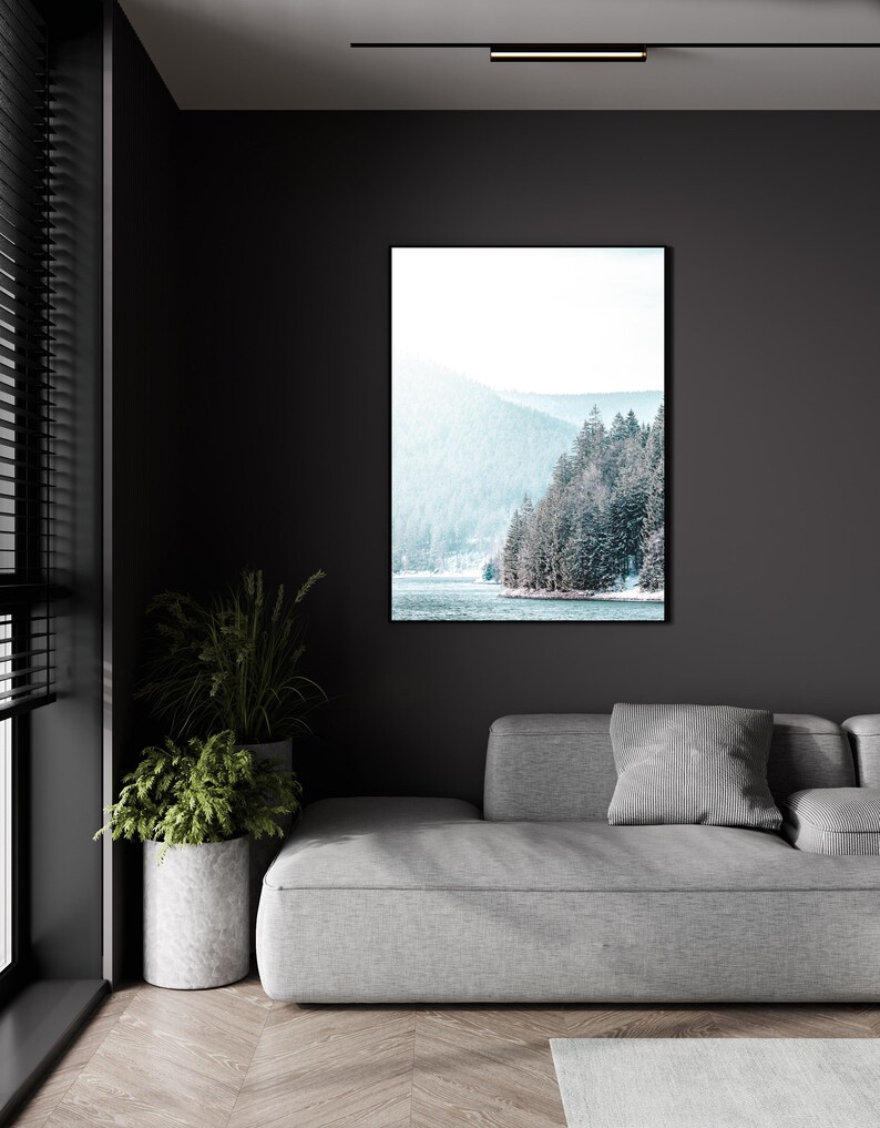 Pode incluir: Uma fotografia emoldurada de uma paisagem montanhosa nevada com um lago em primeiro plano. A foto est&aacute; pendurada em uma parede escura acima de um sof&aacute; cinza.