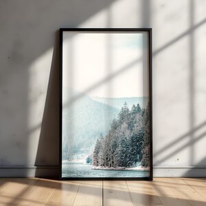 Pode incluir: Uma fotografia emoldurada de uma paisagem montanhosa nevada com um lago em primeiro plano. A foto est&aacute; em uma moldura preta e est&aacute; pendurada em uma parede branca.