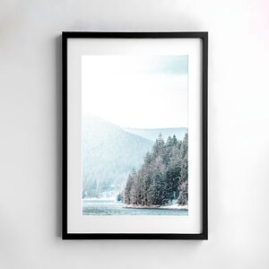 Pode incluir: Uma fotografia emoldurada de uma cena de floresta nevada com um lago em primeiro plano. As &aacute;rvores est&atilde;o cobertas de neve e o lago &eacute; de cor azul claro. O c&eacute;u &eacute; de cor azul claro e h&aacute; nuvens no c&eacute;u.
