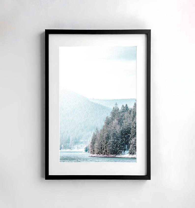 Pode incluir: Uma fotografia emoldurada de uma cena de floresta nevada com um lago em primeiro plano. As &aacute;rvores est&atilde;o cobertas de neve e o lago &eacute; de cor azul claro. O c&eacute;u &eacute; de cor azul claro e h&aacute; nuvens no c&eacute;u.