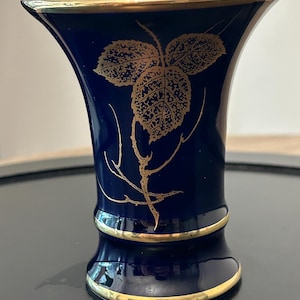 May include: A deep cobalt blue vase with a flared rim and a white interior. The exterior features a delicate gold leaf pattern and thin branch design. The base and the rim are accented with a thin, polished gold band, creating a refined look.