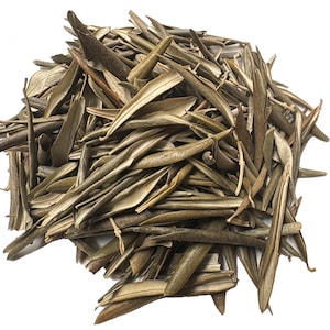 Puede incluir: Un montón de hojas de olivo secas, que muestran una mezcla de tonos verde oliva y marrón. Las hojas son alargadas y delgadas, con venas y texturas visibles. La imagen está sobre un fondo blanco liso, resaltando los colores naturales y los detalles de las hojas.