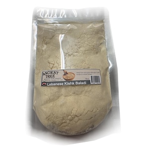 Op de afbeelding: Een transparante plastic zak gevuld met een beige poeder. De zak heeft een etiket met de tekst "ANCIENT TREE" en "Lebanese Kishk Baladi". Het etiket vermeldt ook dat het product uit Libanon is geïmporteerd en 227 gram bevat.
