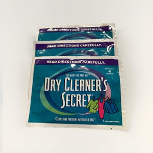 May include: Three packets of Dry Cleaner's Secret laundry detergent. The packets are teal and white with the text "READ DIRECTIONS CAREFULLY" and "DRY CLEANER'S SECRET". The packets also show illustrations of clothing.