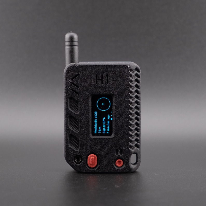 Pode incluir: Um dispositivo port&aacute;til preto com uma pequena antena, uma tela que mostra "H1" e o texto "Meshdistanz 4828 7 km Signal 67% 7 minutes ago".