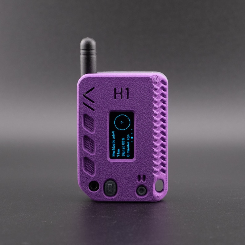 Pode incluir: Um dispositivo de r&aacute;dio port&aacute;til roxo com uma antena preta. O ecr&atilde; mostra "MeshRadio ad-hoc 7km Sinal 80% H&aacute; 8 minutos". O dispositivo tem uma superf&iacute;cie texturizada e o texto "H1" est&aacute; impresso na frente.
