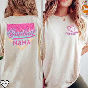 May include: A white t-shirt with a pink and blue baseball graphic on the back that says "Baseball Mama". The front of the shirt has a pink heart with a baseball inside and the text "Jackson".