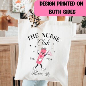 May include: White canvas tote bag with a black and pink design. The design features a cartoon band-aid character with the text "The Nurse Club Est. 2024 Nicole, RN".