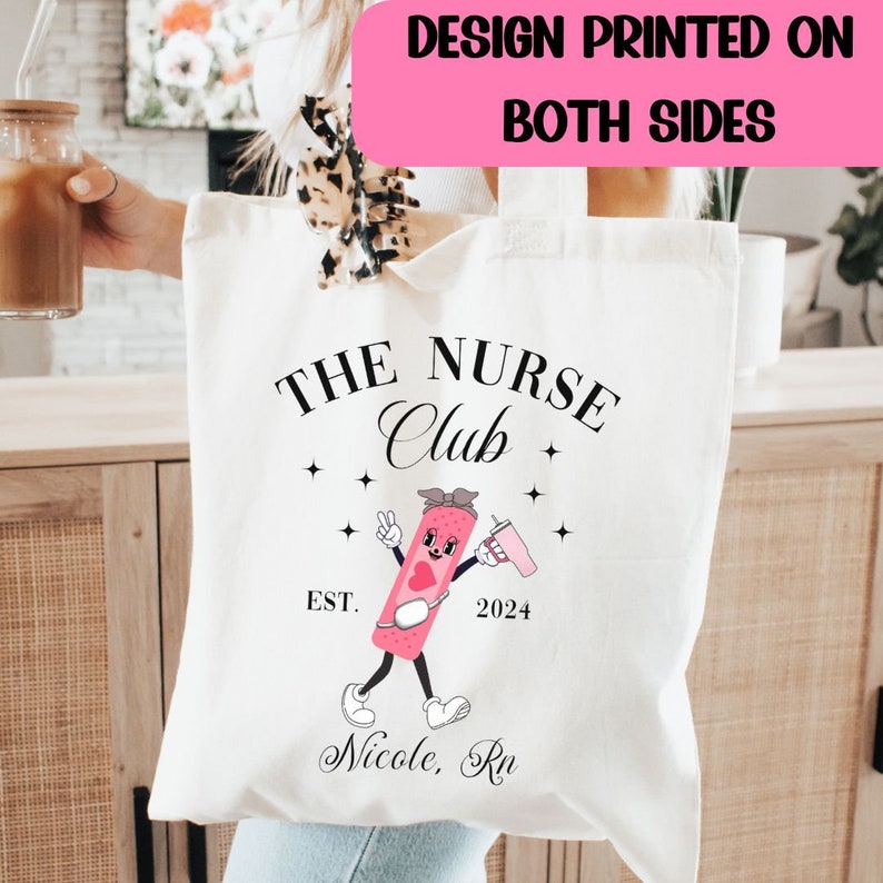 May include: White canvas tote bag with a black and pink design. The design features a cartoon band-aid character with the text "The Nurse Club Est. 2024 Nicole, RN".