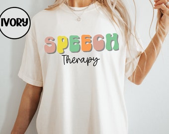 May include: A white t-shirt with the words "SPEECH THERAPY" printed in colorful, retro-style letters.