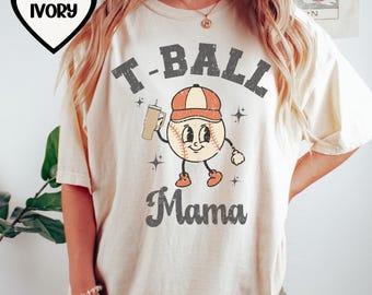 May include: A cream colored t-shirt with a cartoon baseball character holding a drink and the text "T-BALL Mama".