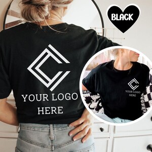 K&ouml;nnte beinhalten: Schwarzes T-Shirt mit einem wei&szlig;en geometrischen Logo-Design auf der R&uuml;ckseite und der Vorderseite. Der Text "YOUR LOGO HERE" ist unter dem Logo auf der R&uuml;ckseite aufgedruckt. Eine herzf&ouml;rmige Grafik mit dem Wort "BLACK" befindet sich in der oberen rechten Ecke.