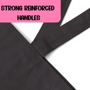 May include: Close-up of the reinforced handles of a black tote bag. The handles are stitched together with strong stitching.