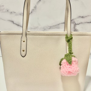 May include: A white leather tote bag with a crocheted pink rose charm attached to the handle.