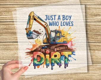 May include: DTF transfer featuring a colorful excavator illustration with the text "JUST A BOY WHO LOVES DIRT." The design includes vibrant paint splatters and the words "READY TO PRESS" at the bottom. The top text reads "CUSTOM DTF TRANSFER."