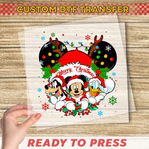 May include: A clear DTF transfer featuring Mickey Mouse, Goofy, and Donald Duck in Santa hats, with the words "Merry Christmas." The design includes snowflakes and Christmas lights. The text "READY TO PRESS" is at the bottom.