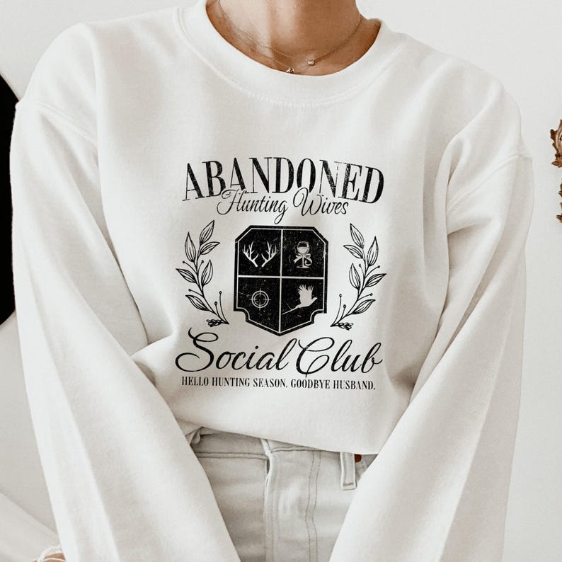 Puede incluir: Sudadera blanca con texto negro que dice "Abandoned Hunting Wives Social Club. Hello Hunting Season, Goodbye Husband."