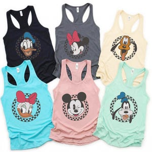 Puede incluir: Seis camisetas sin mangas de tirantes en varios colores, cada una con un personaje diferente de Disney. Los personajes incluyen Pato Donald, Minnie Mouse, Pluto, Daisy, Mickey Mouse y Goofy, todos dentro de un círculo a cuadros.