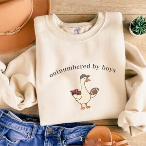 "Outnumbered by Boys Duck Sweatshirt, Funny Mom Shirt with Football and Truck Design, Personalized Family Apparel, Casual Gift for Mom" Outnumbered by boys, Funny mom sweatshirt, Personalized family tee, Duck graphic shirt, Football mom shirt, Truck design sweatshirt, Family gift idea, Mom shirt with kids, Cute mom sweater, Family matching shir, Casual mom outfit, Custom mom apparel, Funny family sweatshirt,
