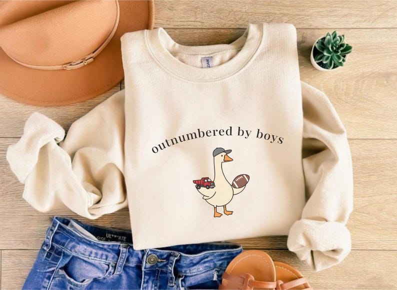 "Outnumbered by Boys Duck Sweatshirt, Funny Mom Shirt with Football and Truck Design, Personalized Family Apparel, Casual Gift for Mom" Outnumbered by boys, Funny mom sweatshirt, Personalized family tee, Duck graphic shirt, Football mom shirt, Truck design sweatshirt, Family gift idea, Mom shirt with kids, Cute mom sweater, Family matching shir, Casual mom outfit, Custom mom apparel, Funny family sweatshirt,