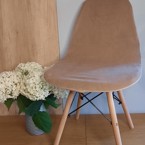 Op de afbeelding: Een beige fluwelen stoel met een zwart metalen frame en houten poten. De stoel staat op een houten vloer.