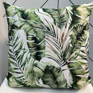 May include: Square throw pillow featuring a lush tropical leaf print in shades of green and brown on a white background. The pillow has a soft, textured appearance, perfect for adding a touch of nature-inspired decor to any room.