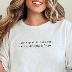 May include: White t-shirt with the text "i can explain it to you but i can't understand it for you." The shirt is paired with light blue ripped jeans. A gold bracelet is visible on the wrist.