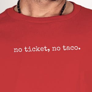 Puede incluir: Camiseta roja de cuello redondo con el texto blanco "no ticket, no taco". La camiseta de manga corta es de color rojo liso. La imagen muestra la parte superior del cuerpo de una persona que lleva la camiseta.