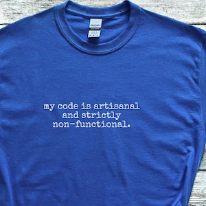 May include: Royal blue t-shirt with the text "my code is artisanal and strictly non-functional." The shirt is paired with black and white sneakers and denim shorts. A straw hat and watch are also in the image.