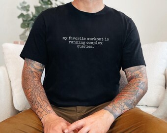 Op de afbeelding: Een zwart T-shirt met korte mouwen en witte tekst in typemachine-stijl in het midden op de borst met de tekst: "my favorite workout is running complex queries." Het shirt heeft een ronde hals en een standaard pasvorm van zwarte stof.