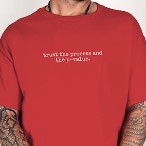 Może przedstawiać: Jaskrawoczerwony T-shirt z krótkim rękawem z białym napisem na piersi: "trust the process and the p-value." Koszulka ma klasyczny okrągły dekolt i prosty, jednolity kolor na całej przedniej części.