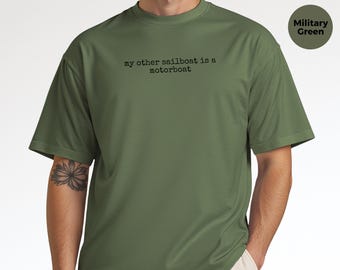 May include: A military green short-sleeved t-shirt featuring the black typewriter-style text "my other sailboat is a motorboat" printed on the chest. The garment has a crew neckline and a standard fit, showcasing a solid color design.