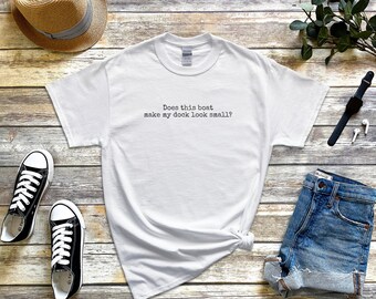 Op de afbeelding: Een wit T-shirt met korte mouwen en de zwarte tekst Does this boat make my dock look small? Het shirt wordt getoond naast een strooien hoed, zwarte sneakers, een blauwe spijkerbroekshort, een zwart polshorloge en witte draadloze oortjes.