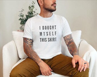 May include: A white short-sleeved t-shirt featuring the black text I BOUGHT MYSELF THIS SHIRT printed in a bold, sans-serif font across the chest. The garment has a crew neckline and a standard fit, constructed from a plain white fabric.