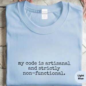 May include: A light blue crew neck t-shirt featuring the black text "my code is artisanal and strictly non-functional." The shirt has a Gildan brand label at the inner neckline and a short-sleeved design made of a solid-colored cotton fabric.