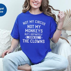 May include: A royal blue short-sleeved t-shirt featuring white text that reads: NOT MY CIRCUS NOT MY MONKEYS BUT I DEFINITELY KNOW ALL THE CLOWNS. The shirt has a crew neckline and a relaxed fit, with a small blue circular icon in the top corner.