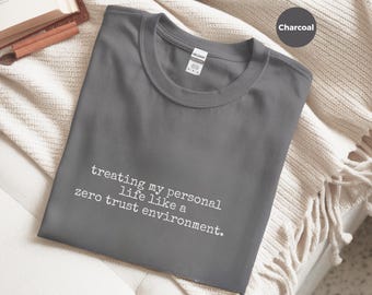 May include: A charcoal gray crew neck t-shirt featuring white typewriter-style text that reads, treating my personal life like a zero trust environment. The shirt has a standard collar and a visible brand label at the inner neckline.