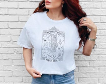 May include: A white short-sleeved t-shirt featuring a black line art graphic of a stack of books inside an ornate frame. The text reads "MURDER MYSTERY SOLVER" and "MYSTERY GUILD" with small illustrations of a magnifying glass, pipe, and cup.
