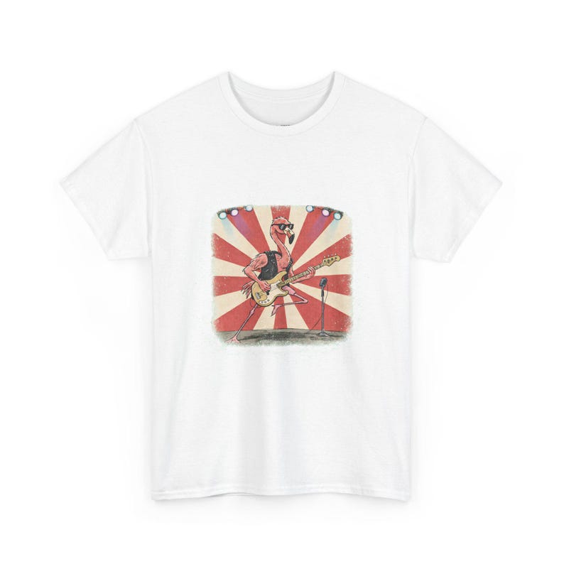 May include: Military green t-shirt featuring a cartoon flamingo playing a bass guitar on a stage with a red and white sunburst background. The flamingo wears sunglasses and a black vest. A microphone stands nearby.