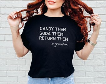 May include: A black short-sleeved t-shirt featuring the white text CANDY THEM SODA THEM RETURN THEM followed by the hashtag #grandma in a cursive script font. The shirt has a crew neckline and a standard fit.