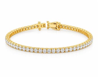 May include: A gold tennis bracelet featuring a continuous row of round, clear, faceted stones set in a polished yellow gold metal frame. The bracelet includes a secure box clasp mechanism with a safety latch, creating a circular shape.