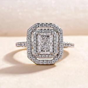 May include: A silver engagement ring with a large, rectangular, clear diamond center stone surrounded by two rows of smaller diamonds.