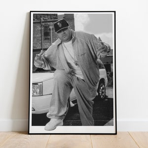 May include: Black and white framed print featuring a person in a casual outfit, leaning against a white SUV. The person is wearing a baseball cap, a jacket, and pants. The background includes a building and a street.