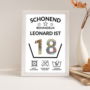 May include: A white framed print with black text that reads "Schonend behandeln Leonard ist 18" with a graphic of the number 18 made of euro bills inside a washing instruction symbol. Below the number are three washing instructions symbols with text that reads "Nicht Schleudern", "Falten Nicht Bugelbar", and "Tagliche Handwasche".