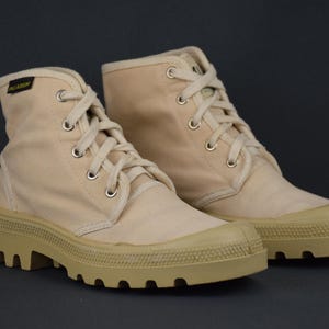 Puede incluir: Un par de botas altas de lona beige con suelas gruesas y robustas. Las botas tienen cordones blancos y est&aacute;n hechas de una tela suave y transpirable.