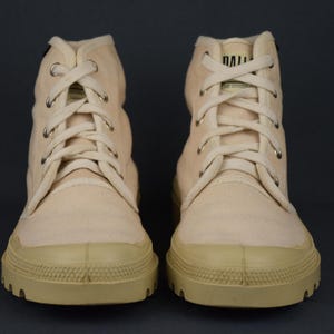 Puede incluir: Un par de zapatillas de lona de color blanco roto de ca&ntilde;a alta con una suela gruesa de goma. Los cordones son blancos y las zapatillas tienen un aspecto ligeramente desgastado.