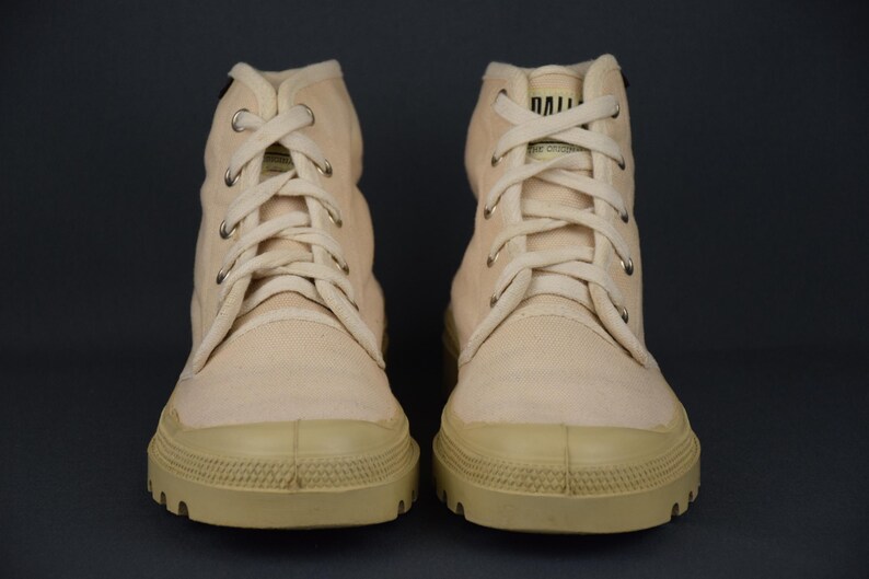 Puede incluir: Un par de zapatillas de lona de color blanco roto de ca&ntilde;a alta con una suela gruesa de goma. Los cordones son blancos y las zapatillas tienen un aspecto ligeramente desgastado.